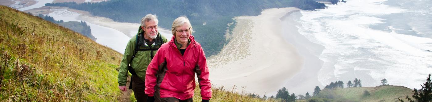 A couple walk along a mountain side trail overlooking the Pacific ocean on the Oregon coast